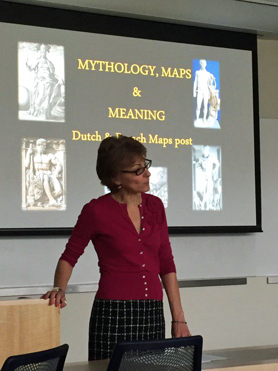 Woman speaking before a Powerpoint slide that reads Mythology & Meaning