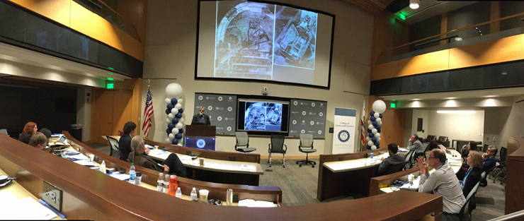 Panorama of audience with man speaking at front of room